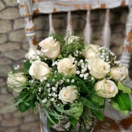 Round arrangement of ivory roses and baby's breath in a glass vase on a rustic white chair