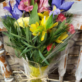 Mixed bouquet of yellow, pink, and purple flowers wrapped in clear cellophane with a twine bow