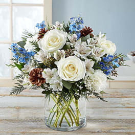 White roses and blue flowers arranged in a clear glass vase