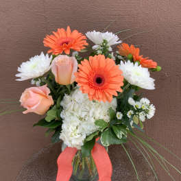 Bouquet of orange gerbera daisies, white mums, and peach roses in a glass vase