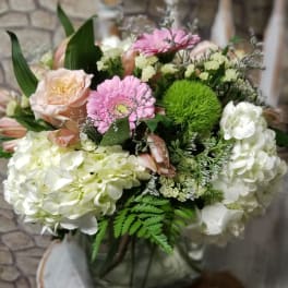 White hydrangeas with pink gerbera, peach rose, and green mums in a square glass vase
