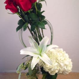 Red roses with a white lily and white hydrangea in a glass vase