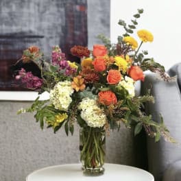 Mixed bouquet of orange roses, yellow mums, and white hydrangeas in a glass vase