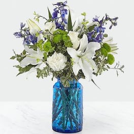 White lilies and blue flowers in a blue glass vase