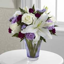 White lilies and roses with purple flowers in a clear glass vase