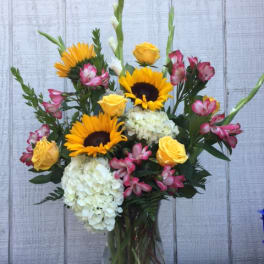 Bouquet of sunflowers, yellow roses, white hydrangeas, and pink alstroemeria in a glass vase