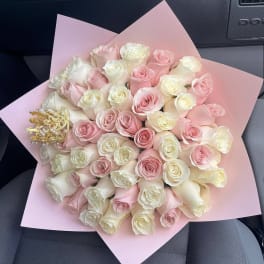 Bouquet of pink and ivory roses wrapped in pink paper with a small decorative crown accent