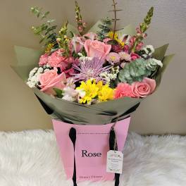 Bouquet of pink roses, yellow daisies, and mixed blooms in pink wrapping