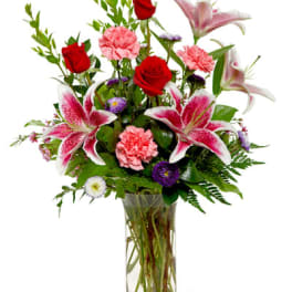 Tall glass vase of red roses, pink lilies and carnations with purple accent flowers