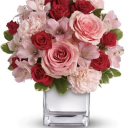 Pink and red roses with pale pink flowers in a clear square vase