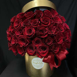 Red roses arranged in a gold hatbox with a red ribbon