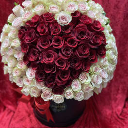 Heart-shaped bouquet of red and pale pink roses in a black box with a red ribbon