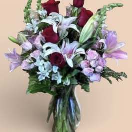 Bouquet of red roses, white lilies, and lavender flowers in a glass vase