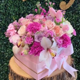 Pink and lavender floral arrangement in a pink box with a ribbon