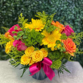 Bouquet of yellow daisies and pink-orange roses in a vase with a magenta ribbon