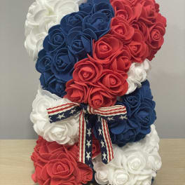 Patriotic teddy bear made of red, white, and blue roses with a ribbon bow