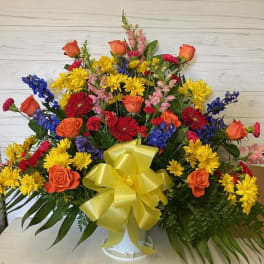 Colorful mixed flower arrangement in a white vase with a yellow bow