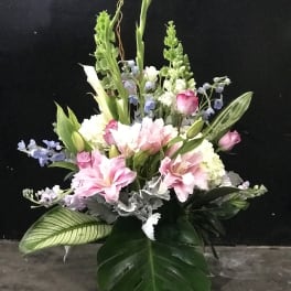 Tall bouquet of pink lilies, white callas, and blue flowers with large tropical leaves