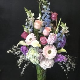 Tall mixed bouquet in a glass vase with pink roses and pastel blooms