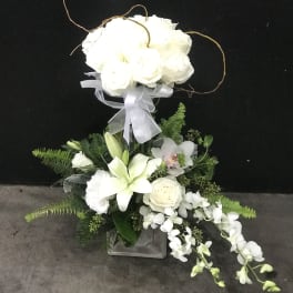 White floral arrangement with lilies, roses, and orchids in a square vase