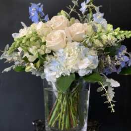 Bouquet of pale roses, hydrangeas, and blue flowers in a clear glass vase