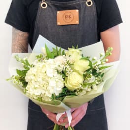 Handheld bouquet of white and pale yellow flowers wrapped in paper