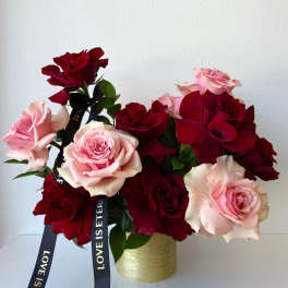 Pink and red roses arranged in a gold vase with black ribbons