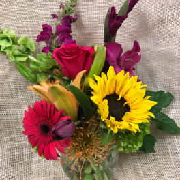 Mixed bouquet in a clear glass vase with a sunflower, rose, and gerbera daisies