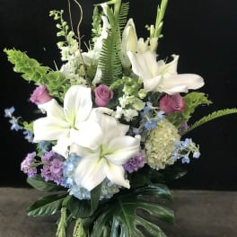 White lilies and pastel flowers arranged in a glass vase