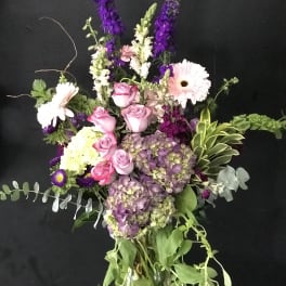 Mixed bouquet with pink roses, hydrangeas, and tall purple blooms in a glass vase