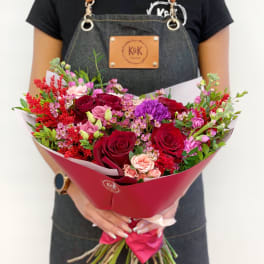 Handheld bouquet of red, pink, and purple roses with mixed filler flowers