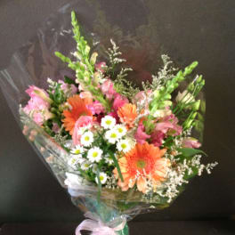 Hand-tied bouquet of orange gerbera, pink roses, and white daisies wrapped in cellophane with a pink bow
