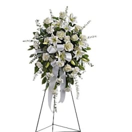 White floral standing spray with lilies, roses, and ribbon on an easel