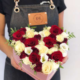 Heart-shaped box of red, white, and cream roses held by a person