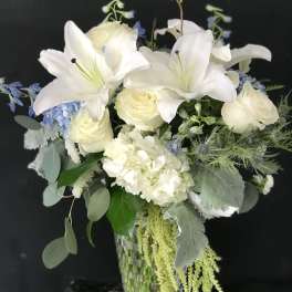White lilies and roses in a glass vase with blue accents