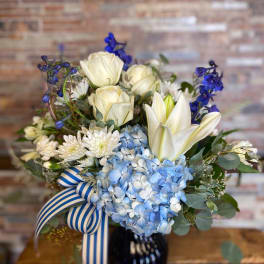Blue and white bouquet with roses, hydrangeas, lilies, and a striped ribbon in a vase