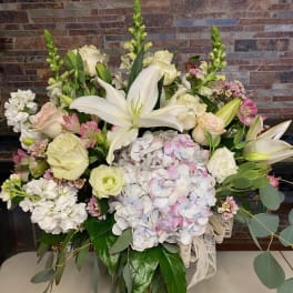 Large bouquet of white lilies, roses, and pastel hydrangeas in a glass vase