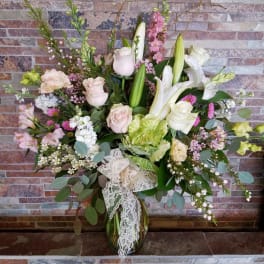 Mixed bouquet of white lilies, pale roses, and pink flowers in a glass vase