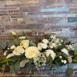 White rose arrangement with greenery against a brick wall