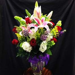 Mixed bouquet of lilies and roses in a glass vase with a purple ribbon