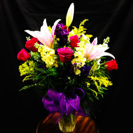 Bouquet of red roses and pink lilies in a glass vase with a purple ribbon