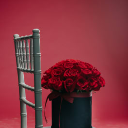 Red rose arrangement in a black hat box on a chair