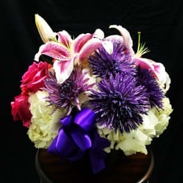 Bouquet of pink lilies, purple flowers, and white blooms with a purple ribbon