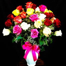 Heart-shaped bouquet of multicolored roses in a white vase with a pink ribbon