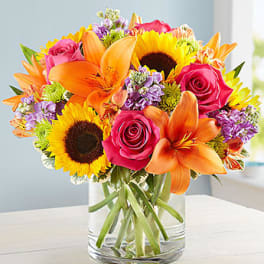 Bouquet of sunflowers, roses, lilies, and purple flowers in a glass vase