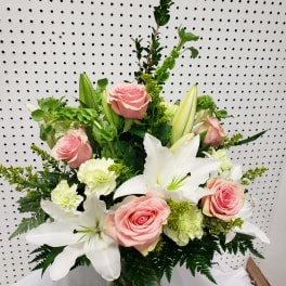 Pink roses and white lilies in a glass vase with green accents