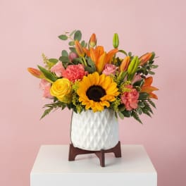 Mixed bouquet with sunflower, lilies, roses, and carnations in a white vase