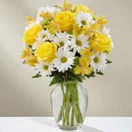 Yellow roses and white daisies in a clear glass vase