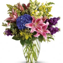 Bouquet of pink lilies, blue hydrangea, and purple flowers in a clear glass vase