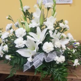 White lilies and carnations in a low arrangement with a silver ribbon